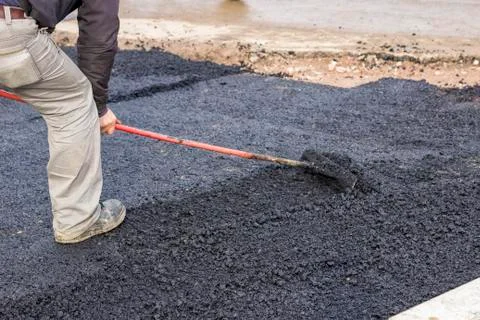Worker using rake to level asphalt pavement Stock Photos