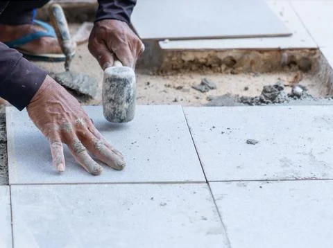 The worker is using a rubber mallet to adjust the level of the floor tiles. Stock Photos