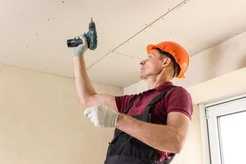 Worker is using screws and a screwdriver to attach plasterboard to the ceilin Stock Photos