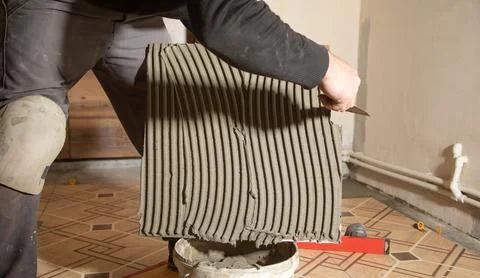 Worker using spatula and putting glue on ceramic tile. Stock Photos