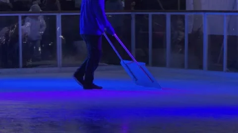 A worker using a specialized shovel to smooth an outdoor ice rink surface at Stock Footage 345665589