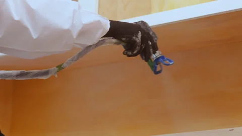 Worker using a sprayer to apply paint or coating inside cabinet during Stock Footage 334019870