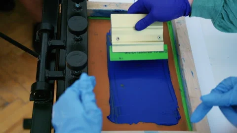 Worker using a squeegee to spread ink across a screen printing frame during Video stock 336878485