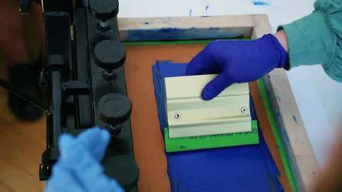 Worker using a squeegee to spread ink across a screen printing frame during Stock Footage 336878559