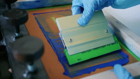 Worker using a squeegee to spread ink across a screen printing frame during Stock Footage 336878859