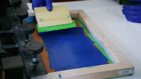 Worker using a squeegee to spread ink across a screen printing frame during Stock Footage 336879203