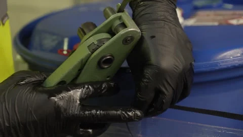 Worker using a strapping tool to secure blue industrial barrels. Professional Vídeo Stock 335351652