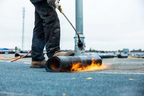Worker Using Torch to Apply Roofing Material on Flat Rooftop Stockfoto's