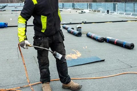 Worker Using Torch on Flat Rooftop with Roofing Materials Nearby Stock Photos