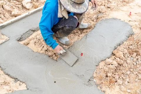 The worker is using a trowel to level the lean concrete surface. Stock Photos
