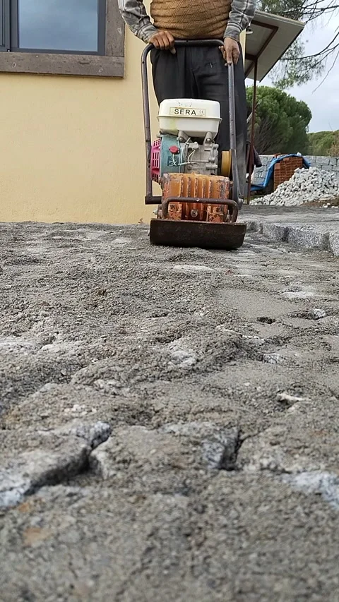 Worker using a vibratory plate compactor to level gravel for a new pavement Stock Footage 334062061