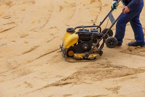 Worker using vibratory plate compactor for compaction sand during path Stockfoto's