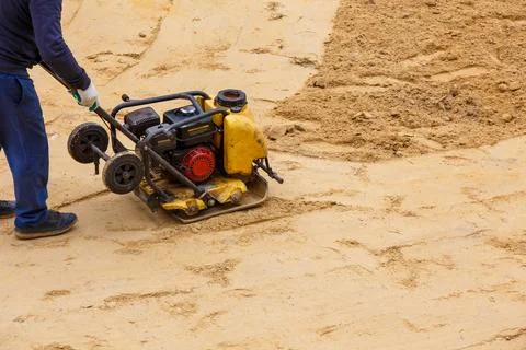 Worker using vibratory plate compactor for compaction sand during path Stock Photos
