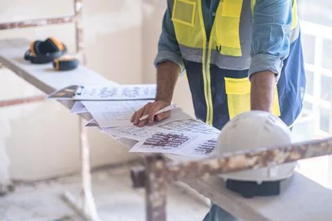 Worker in vest editing and correcting renovation project papers stands by Foto stock