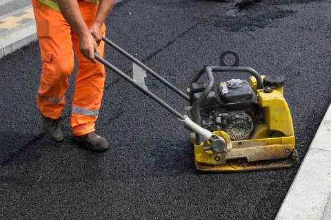 Worker with vibrating compactor plate in action Stock Photos