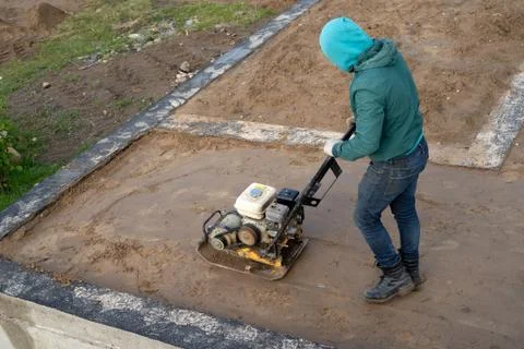 A worker with a vibrating tamping machine rams the ground Stock Photos