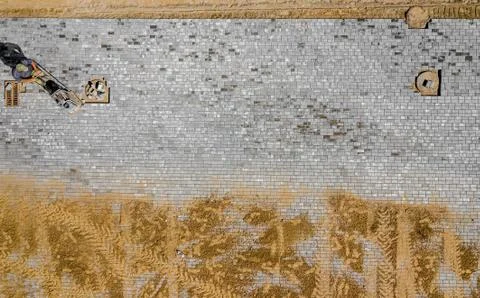 Worker with vibratory plate compactor compacting sand at road or sidewalk con Stock Photos