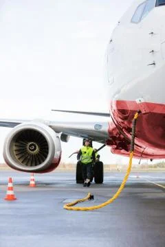 Worker Walking By Airplane Being Charged On Runway 写真素材