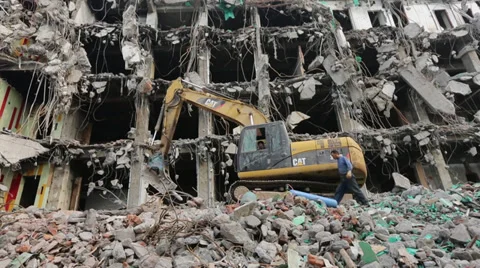 Worker walking next to a demolishing machine on the ruins of city building Stock Footage 35364580