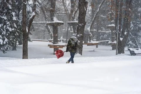 A worker walking through deep snow carrying a red shovel near an aerial rope Stock Photos