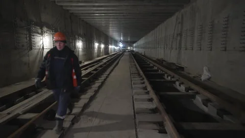 Worker walks between railroad lines in illuminate tunnel Stockbeeldmateriaal 313828534