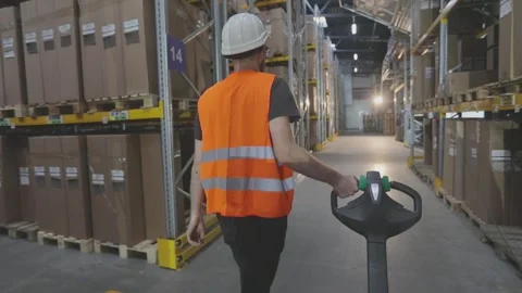 A worker in a warehouse carries a Pallet Stacker Truck with goods. Worker with 库存影片 296319834