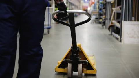 A worker in a warehouse or hardware store uses a hand pallet stacker to Stock Footage 272585997