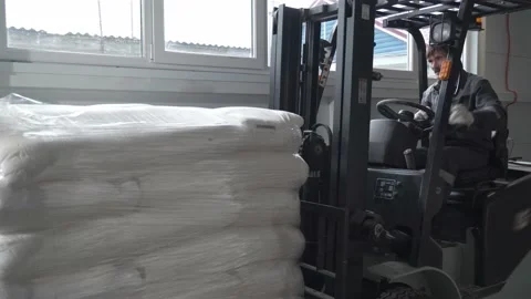 A worker in a warehouse unloads pallets with an electric forklift with sacks of Video stock 235547051