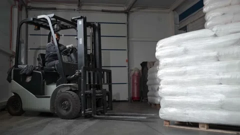 A worker in a warehouse unloads pallets with an electric forklift with sacks of Stock Footage 235931378
