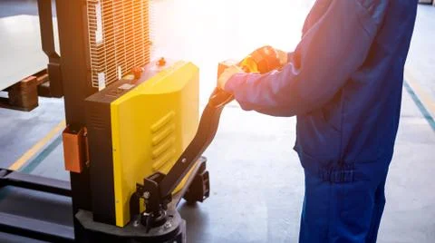 A worker in a warehouse uses a hand pallet stacker to transport pallets. Stock Photos