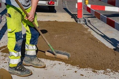 Worker in warning trousers and working shoes scrubbs sand on the street. Stock Photos