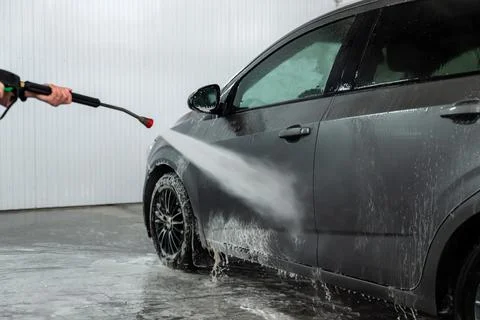 A worker washes off active foam from a car at a car wash. dirty foam Stock Photos