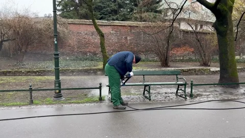 A worker washes a path in a park with a powerful jet of water using a compressor Stock Footage 175357635