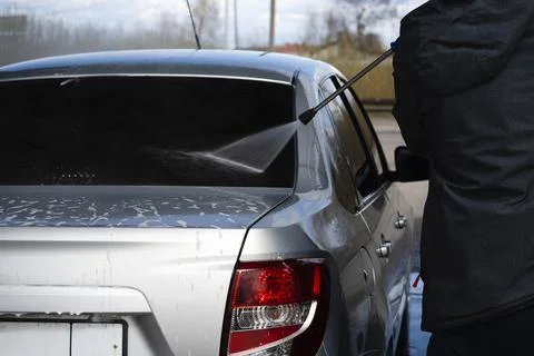 Worker washes the rear window of a gray car Stock Photos