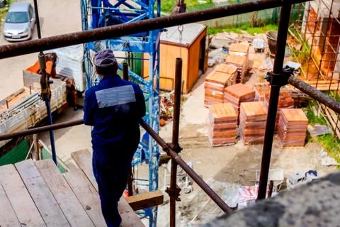 Worker is watching construction site from above, standing on scaffold Stock Photos