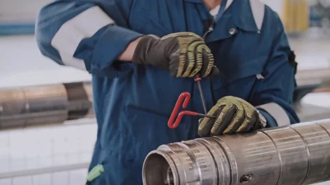 A worker wearing gloves at an enterprise is servicing a drill or an oil pipe. Stock Footage 316320946