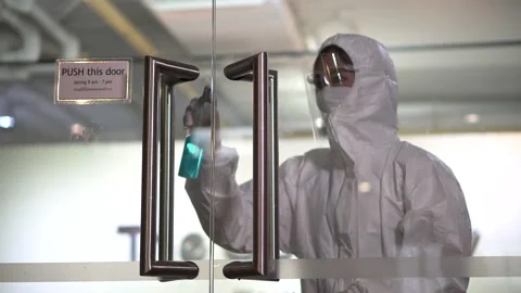 Worker wearing ppe suit using alcohol sanitizer spray to clean the door handl Stock Footage 137951182