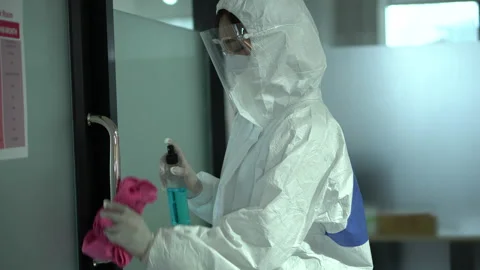 Worker wearing ppe suit using alcohol sanitizer spray to clean the door handl Stock Footage 140125442
