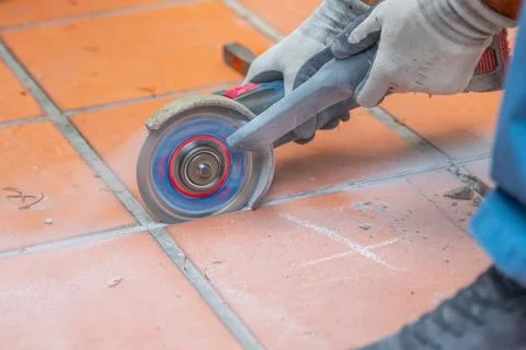 Worker wearing protective gloves cuts ceramic floor tiles with an electric an Stock-Fotos