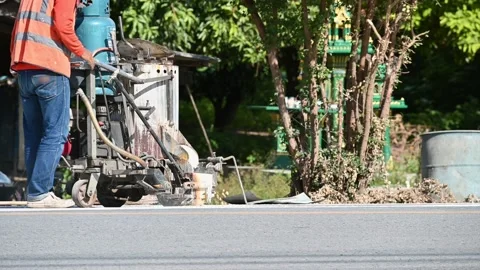 Worker wearing uniform is making the white line on road with painting machine Stock Footage 163982455