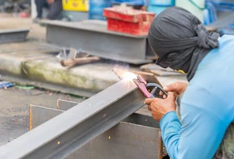 Worker welder without personal protective equipment welding base beam suport. Stock Photos