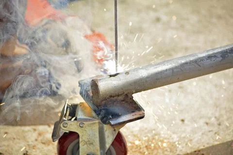 Worker with a welding machine fixing a caster wheels, sparks flying around Stock Photos