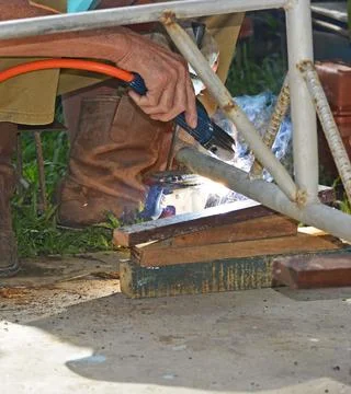 Worker with a welding machine fixing a caster wheels, sparks flying around Stock Photos