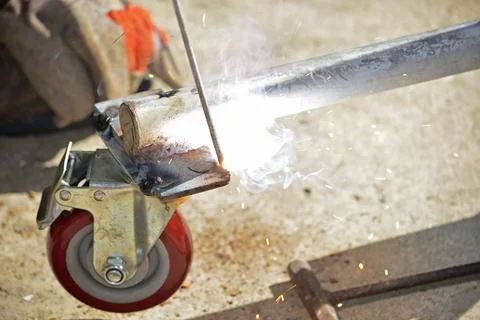 Worker with a welding machine fixing a caster wheels, sparks flying around Foto stock