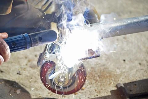 Worker with a welding machine fixing a caster wheels, sparks flying around Stock Photos