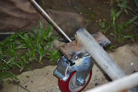 Worker with a welding machine fixing a caster wheels, sparks flying around Stock Photos