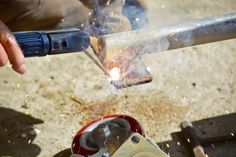 Worker with a welding machine fixing a caster wheels, sparks flying around Stock Photos