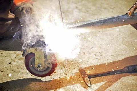 Worker with a welding machine fixing a caster wheels, sparks flying around Stock Photos