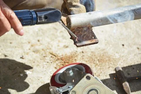 Worker with a welding machine fixing a caster wheels, sparks flying around Stock Photos