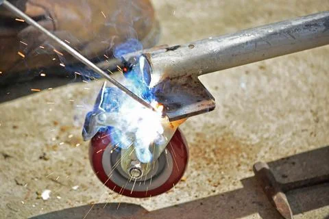 Worker with a welding machine fixing a caster wheels, sparks flying around Foto stock